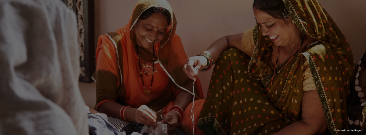 Two women in traditional Indian attire sitting and stitching together.
