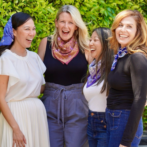 Four women wearing colorful scarves outdoors with greenery in the background